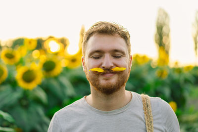 Smiling man with petals on mustache against sunflowers