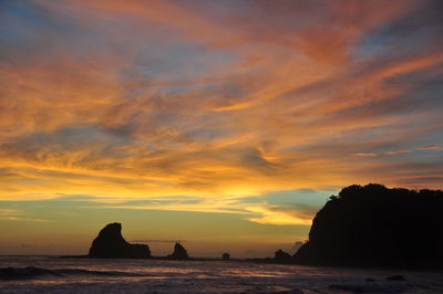 Silhouette rocks on sea against sky during sunset