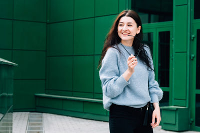 Portrait of smiling young woman standing against wall