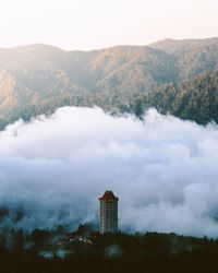 Aerial view of building and clouds by mountains against sky on sunny day