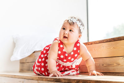 Cute girl looking away while sitting on wood at home