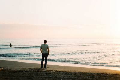 Rear view of man standing at beach against clear sky