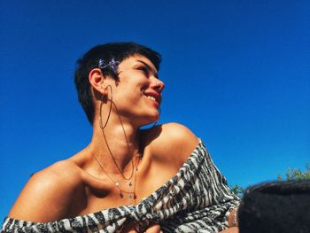 Low angle view of smiling woman looking away against blue sky
