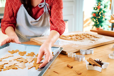 Woman's hands putting cookies a shape of christmas gingerbread on oven paper. 