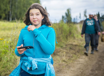 Portrait of teenage girl using smart phone while walking on dirt road