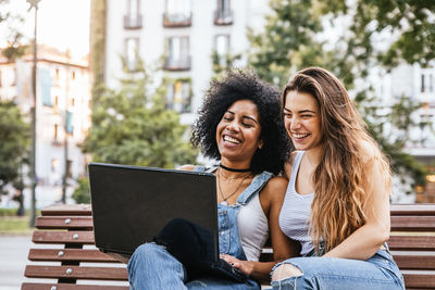 Female friends using laptop while sitting on bench