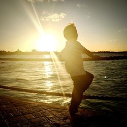 Boy standing at beach against sky during sunset