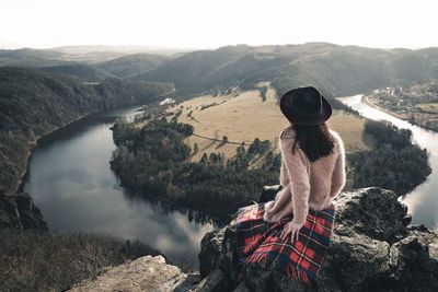 Rear view of woman sitting on cliff against river