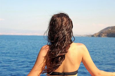 Rear view of woman looking at sea against sky on sunny day