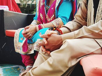 Midsection of bride and groom sitting on chair