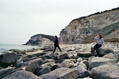 People on rocks by sea against sky