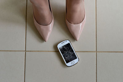 Low section of woman standing by damaged phone on tiled floor