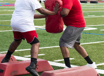 A football player at summer camp hitting his coaches pad while running sideways over red barriers 