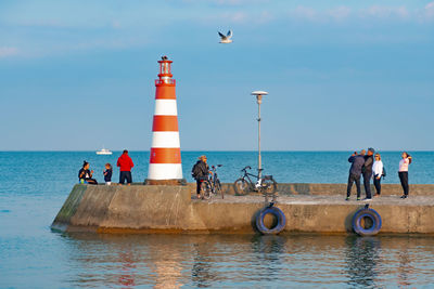 People on lighthouse by sea against sky