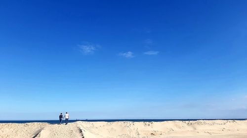 Rear view of couple standing at beach against sky