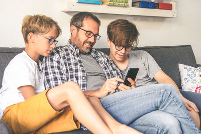 Father with sons sitting on sofa while using mobile phone