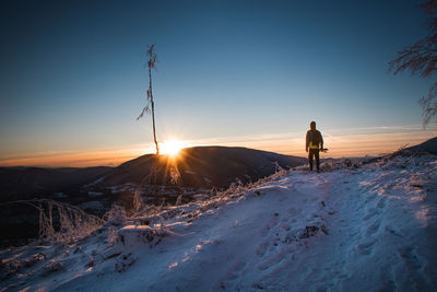 Woman on snow covered land against sky during sunset