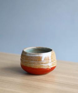 Handmade ceramic cup with red and brown on wooden table