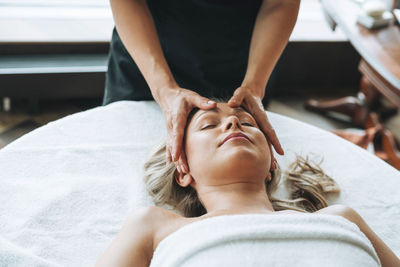 Attractive blonde young woman on couch with white linen enjoys hand facial massage in spa