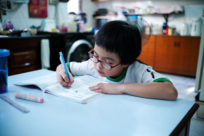 Rear view of boy and book on table