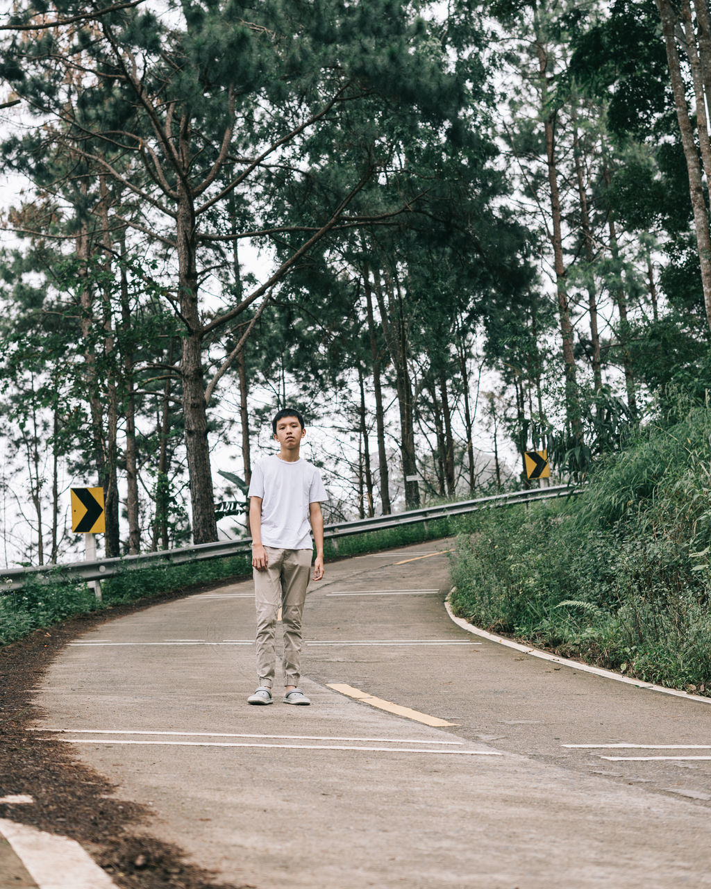 MAN STANDING ON ROAD ALONG PLANTS