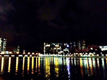Illuminated cityscape by river against sky at night