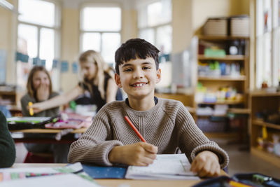 Portrait of happy male pupil sitting at desk in classroom