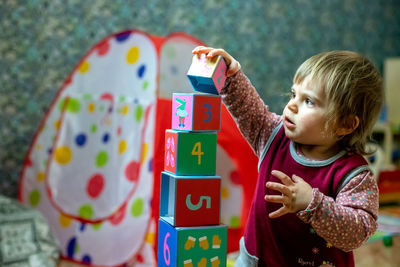 Cute baby girl playing with toy blocks at home