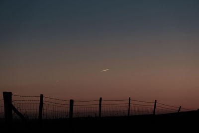 Vapour trails of airplanes at sunset. a silhouette of a barbed wire fence on a hill.