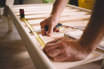 Cropped hands of man measuring wood at home