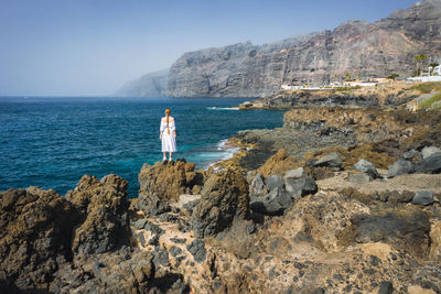 Rear view of woman standing on rock by sea against sky