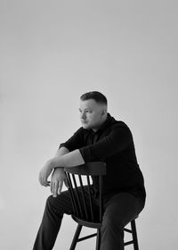 Low angle view of young man sitting on chair against sky