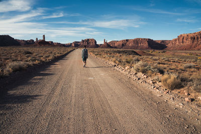 Rear view of man walking on road against sky