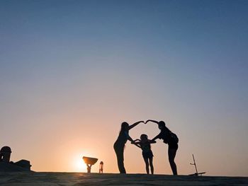 Silhouette people at beach against sky during sunset