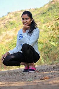 Portrait of young woman crouching on land outdoors