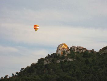 Hot air balloon by trees on cliff against sky