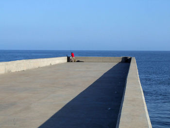 Man standing on pier over sea against blue sky