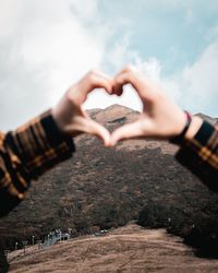 Cropped hands making heart shape against mountain