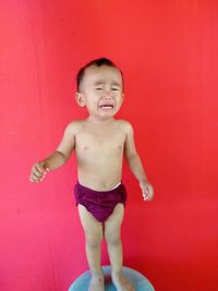 Shirtless boy crying while standing against red wall