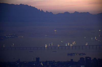 Illuminated boats by rioniteroi bridge in sea against silhouette mountains