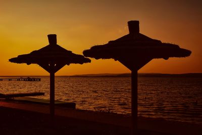 Silhouette gazebo on beach against sky during sunset