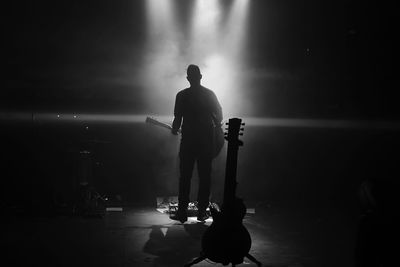 Silhouette man standing with guitar at night