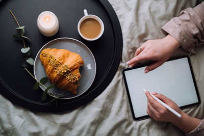 Flat lay, woman using digital tablet for drawing while lying on bed with croissant with cappuccino