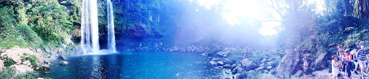 tree, sunlight, water, nature, built structure, growth, sunbeam, panoramic, beauty in nature, building exterior, day, sky, plant, architecture, outdoors, motion, fountain, scenics, no people, sunny