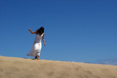 Full length of woman walking on sand at desert against clear sky