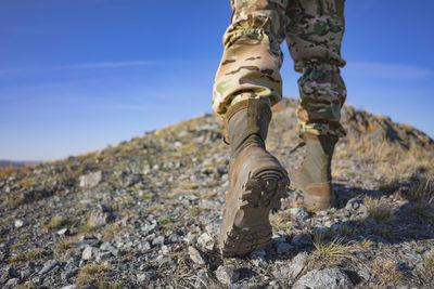 A soldier in camouflage and military boots climbs a mountain. space for text. shallow depth of field