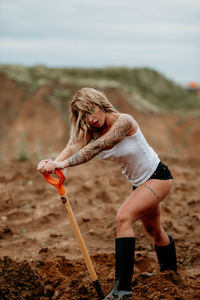 Young woman standing on the sand and digging with a shovel