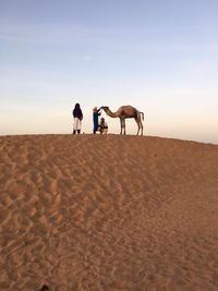 Rear view of people riding on sand at desert against sky