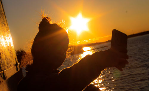 Rear view of man on sea against sky during sunset