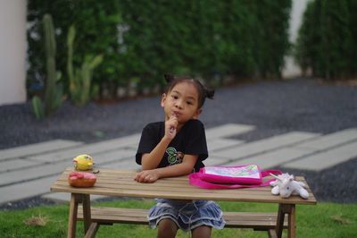 Portrait of girl with spoon in mouth sitting on bench